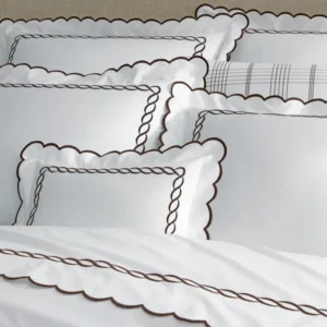 A collection of white bedding with elegant scalloped edges and brown rope-like embroidery, arranged neatly on a bed. Featuring Classic Chain Scallop bedding by Matouk. Available at Linen Society.