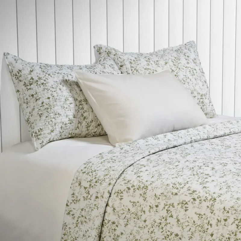 Marjolaine quilt set in white with sage green botanical foliage print, styled on a bed with matching pillow shams