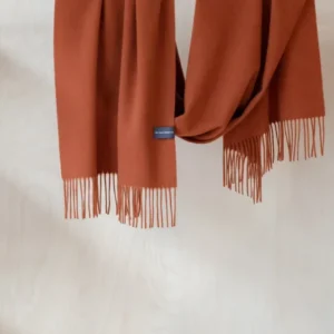 TBCo Lambswool Oversized Scarf in Rust Melange draped over wooden rail, showing soft texture and fringed ends