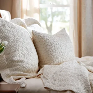 SDH Allegro Jacquard ivory textured decorative pillow on a linen bed near a sunlit window.