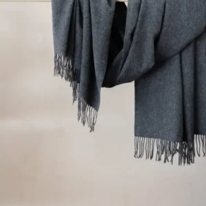Luxurious TBCo charcoal melange cashmere blanket scarf with fringe draped elegantly over wooden rail displaying soft texture
