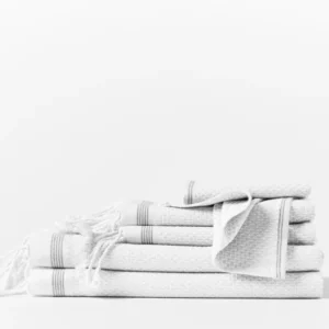 Coyuchi Mediterranean 6-piece white towel set with waffle texture and stripe trim, stacked.
